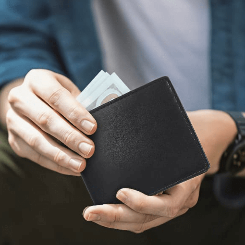 Person holding a black wallet with money against a blurred background