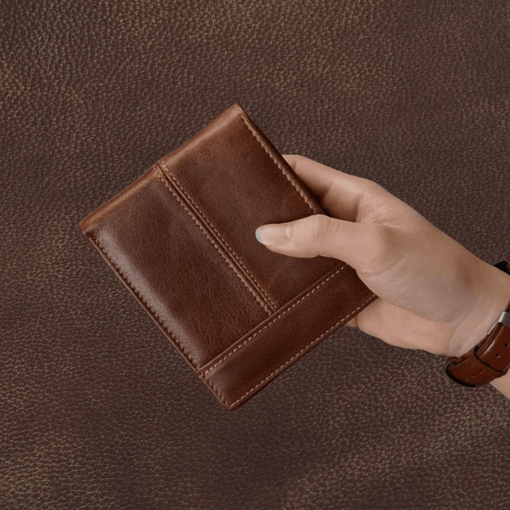Brown leather wallet held by a hand on a brown textured background