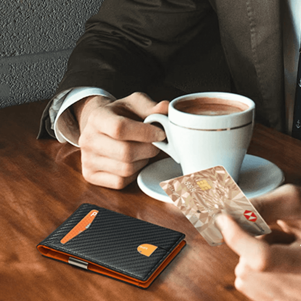 Person holding a cup of coffee with a wallet and cards on a table