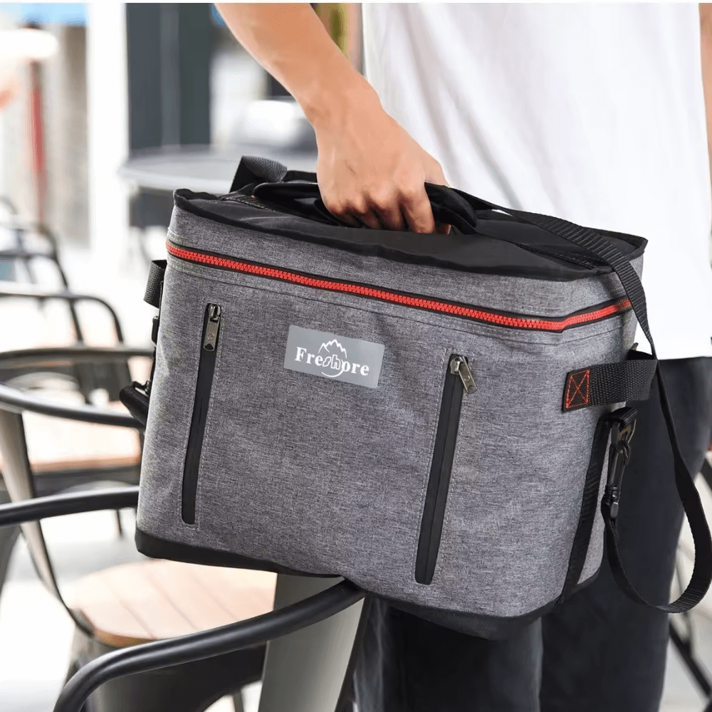 Person holding a gray and black bag with a visible brand logo in an outdoor setting.