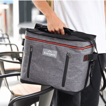 Person holding a gray and black bag with a visible brand logo in an outdoor setting.