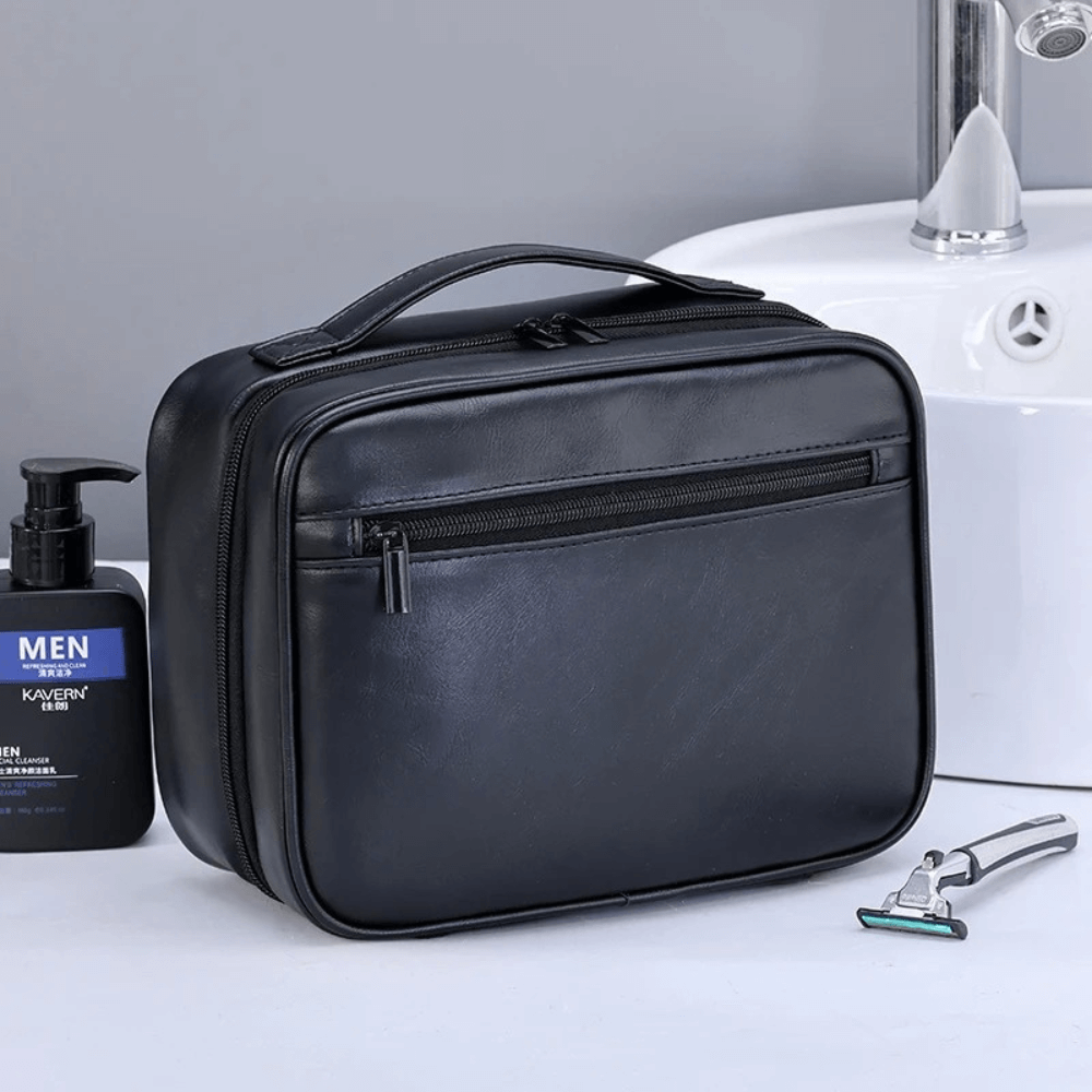 Black toiletry bag on a bathroom counter with a bottle and razor.