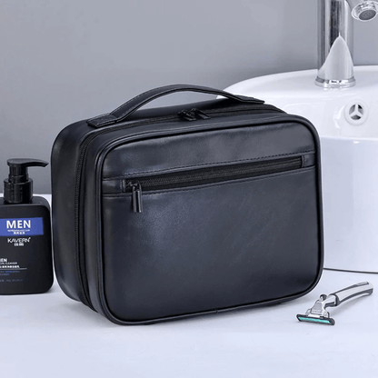 Black toiletry bag on a bathroom counter with a bottle and razor.