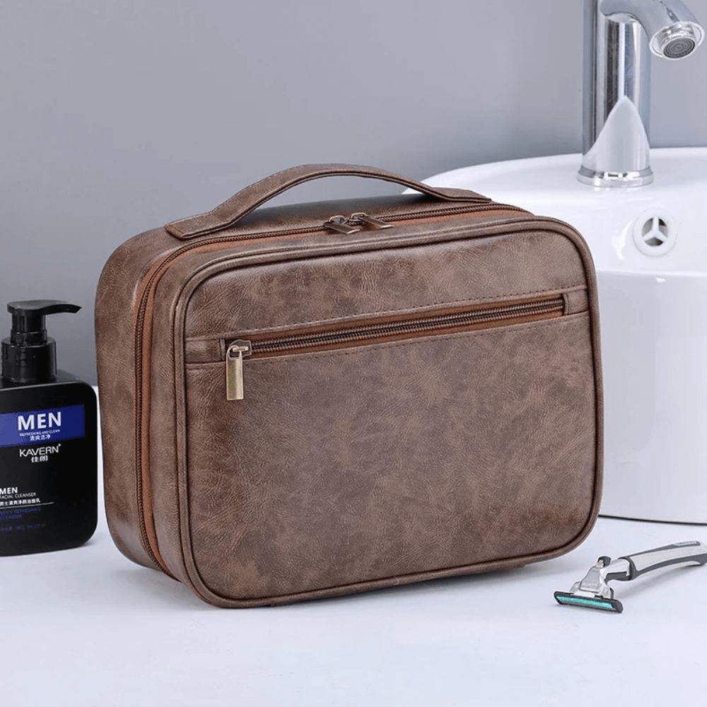 Brown toiletry bag on a bathroom counter with a bottle and razor.