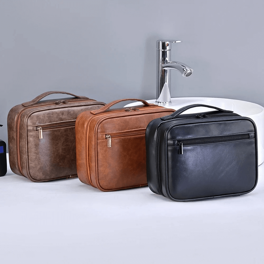Three leather toiletry bags in brown and black on a white surface with a gray background.