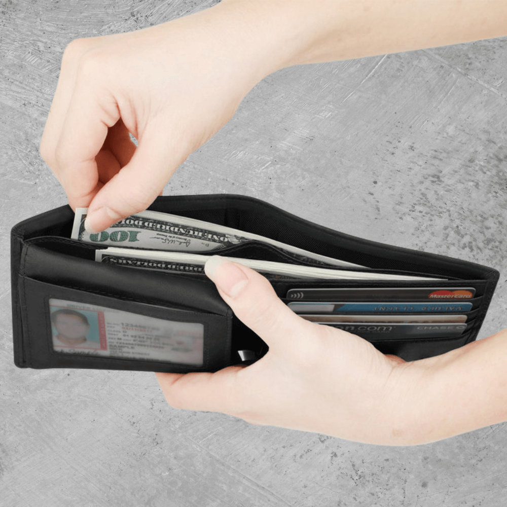 Person holding a black wallet with cards and money on a gray background